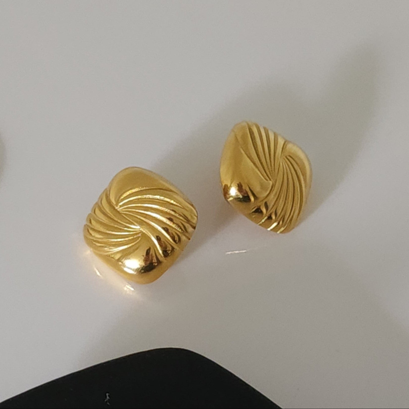 Pair of gold square statement earrings on a grey background.