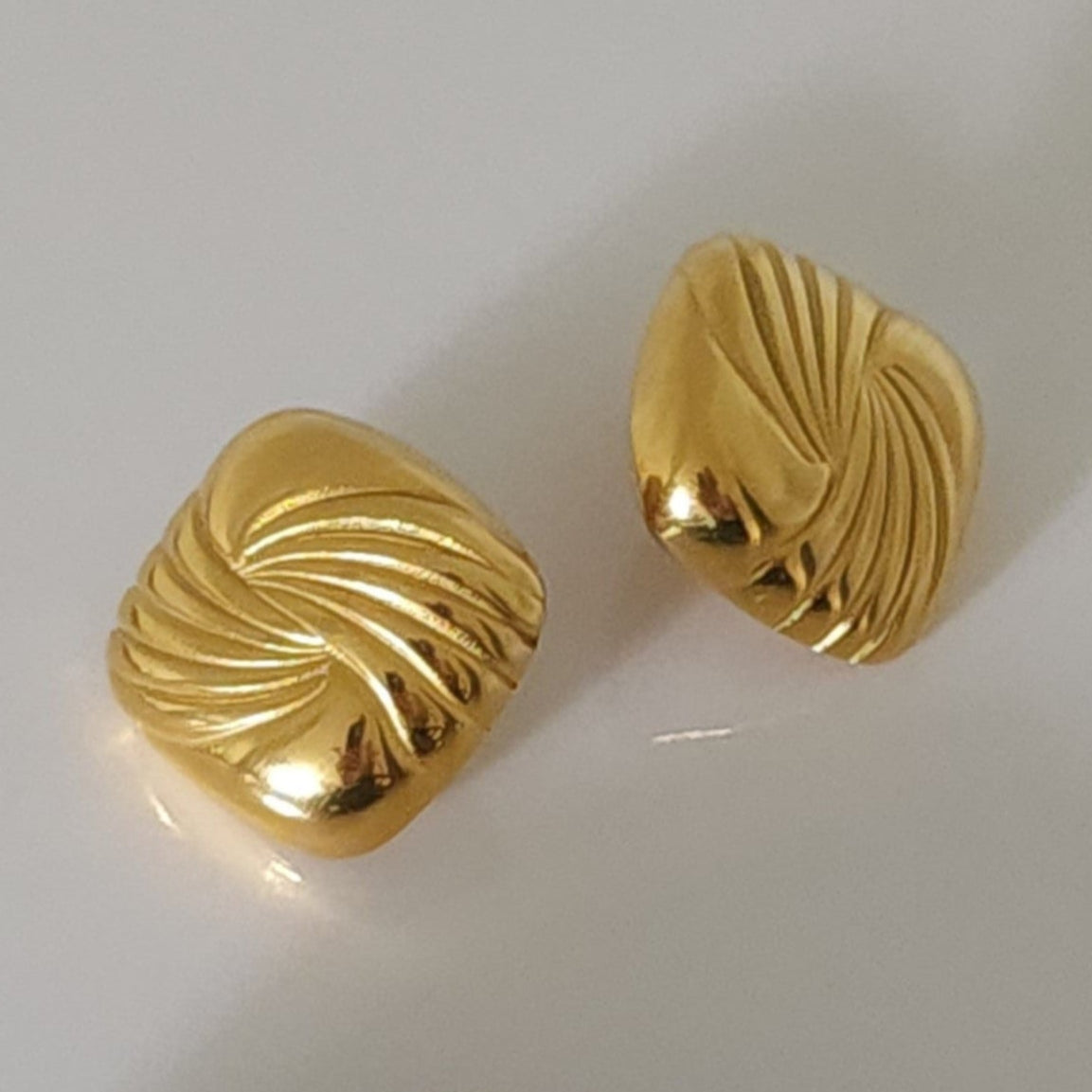 Pair of gold square statement earrings on a grey background.
