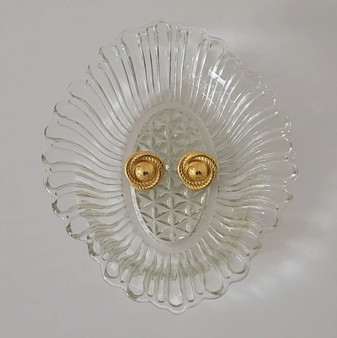 A pair of gold statement earrings on a crystal dish.