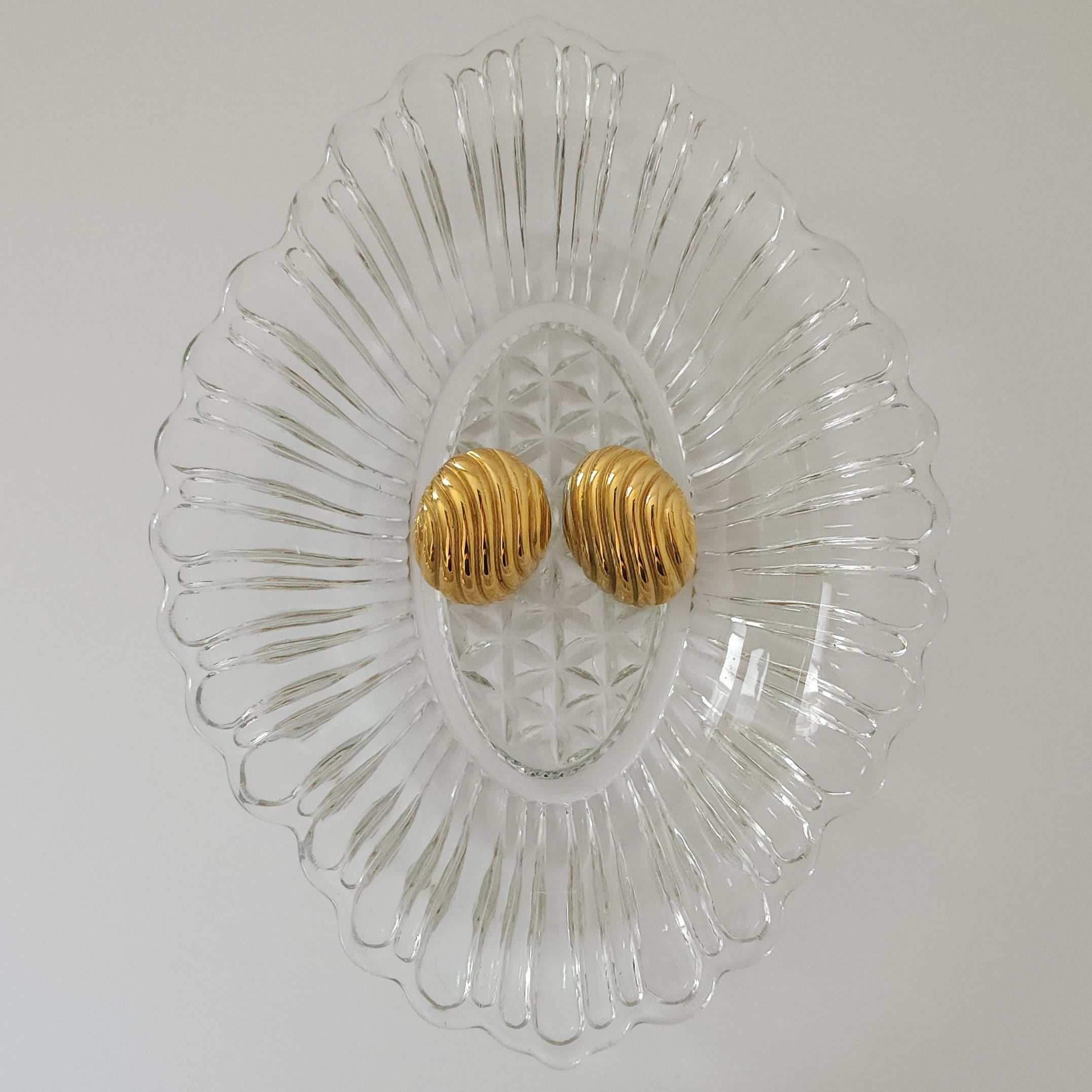 Gold earrings on a decorative glass plate with a plain background