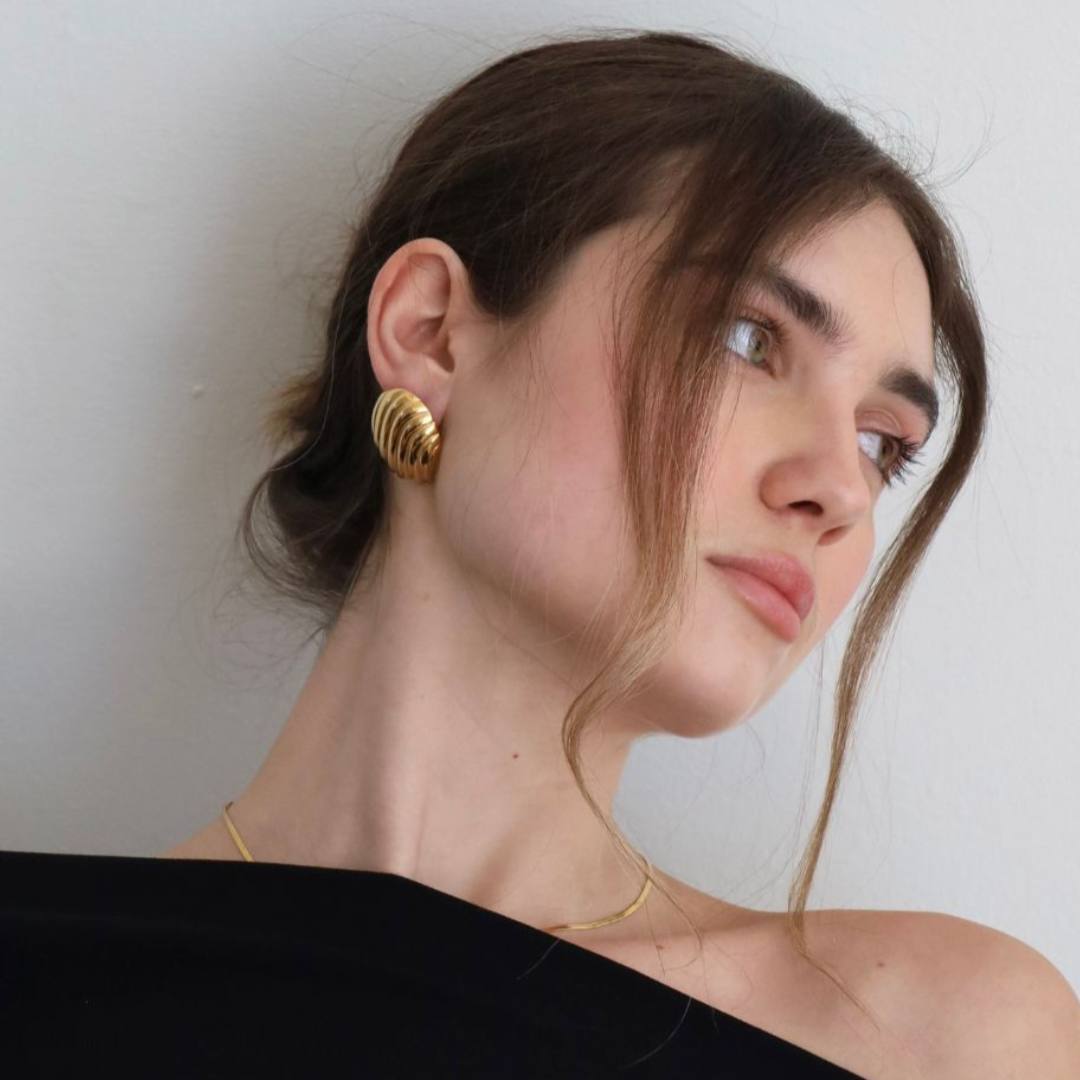 Woman wearing gold oval statement earrings against a plain background