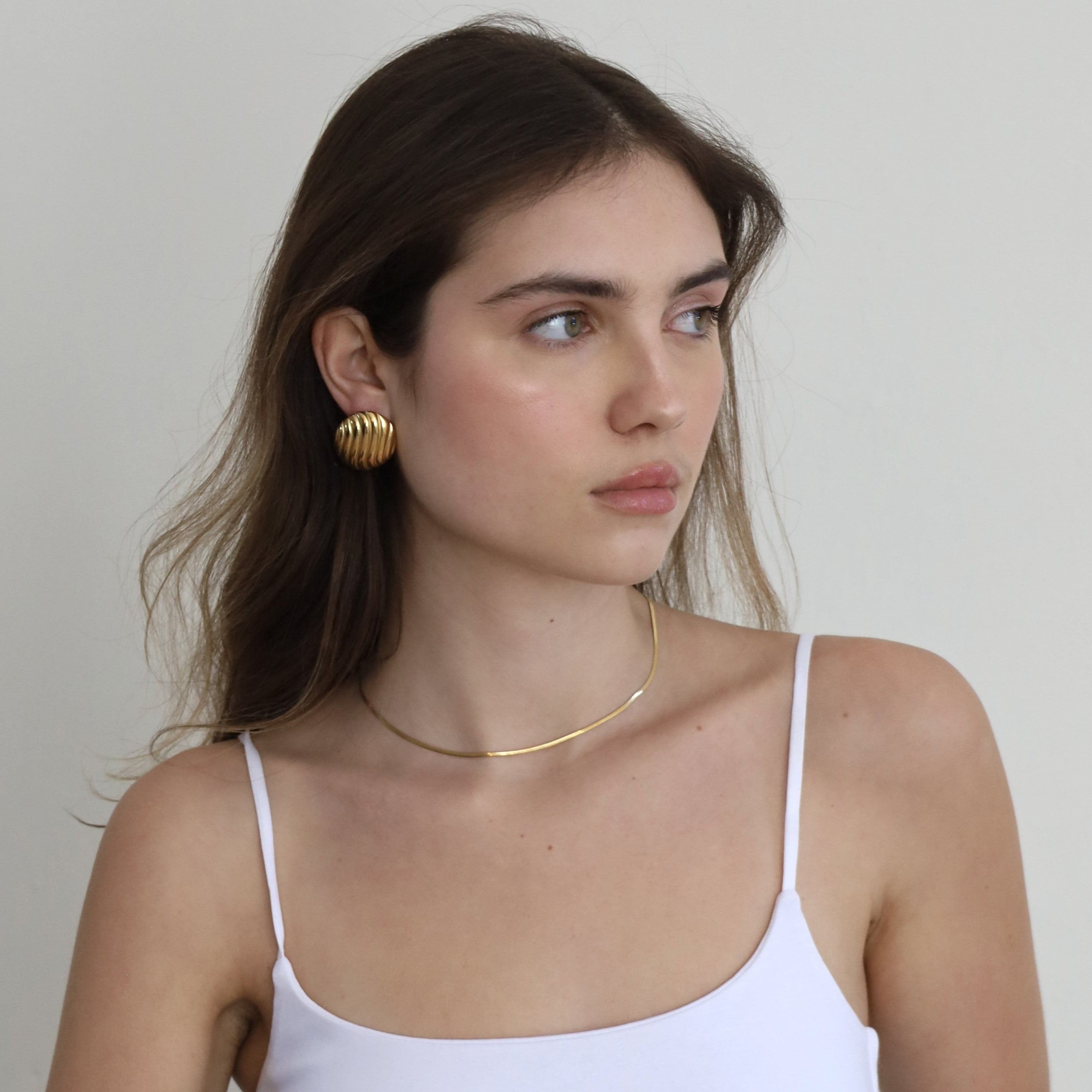 Woman wearing gold earrings and a thin gold necklace against a plain background