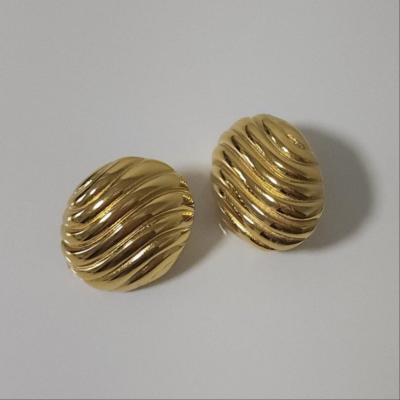 Pair of gold oval statement earrings on a light gray background