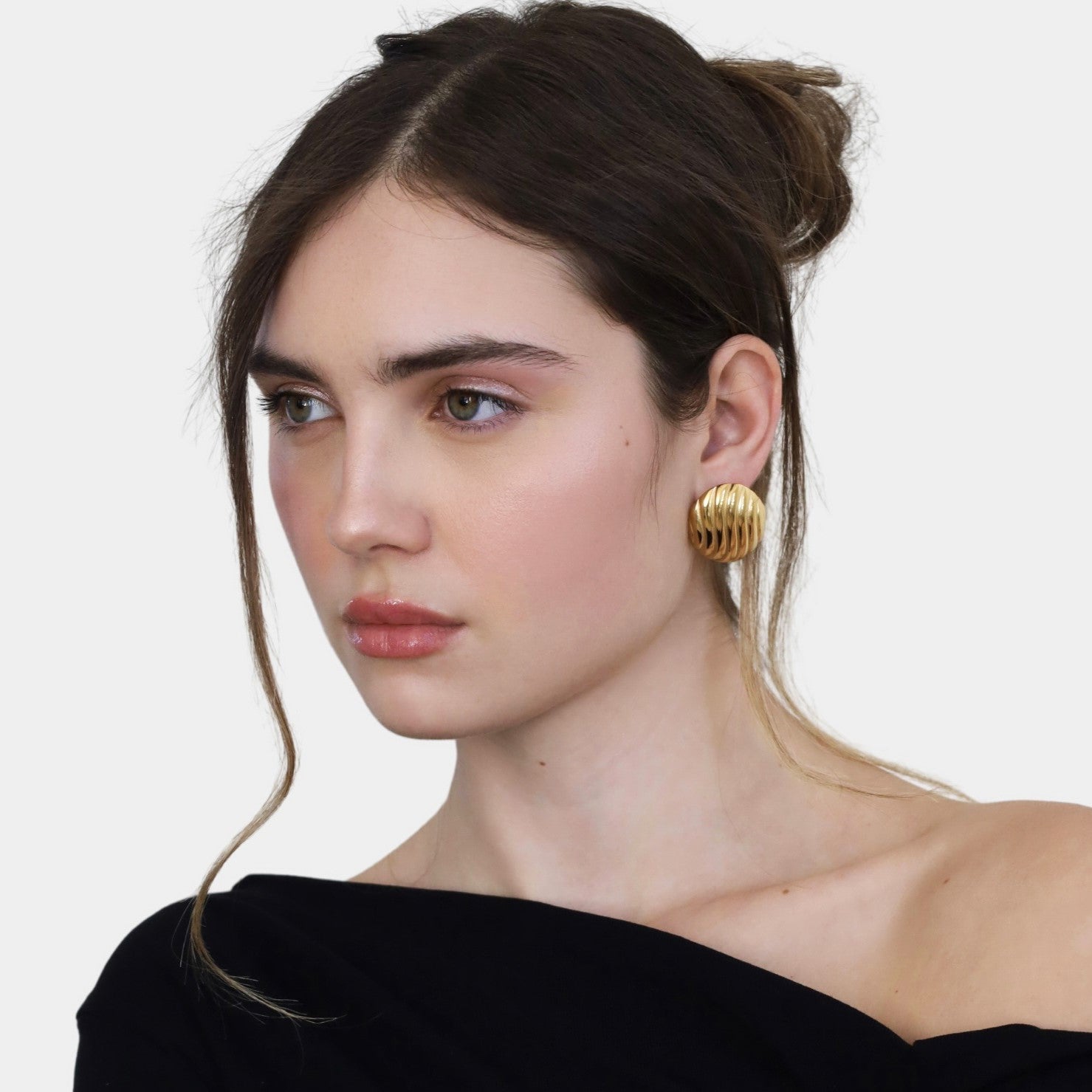 Woman wearing oval gold statement earrings and a black top.