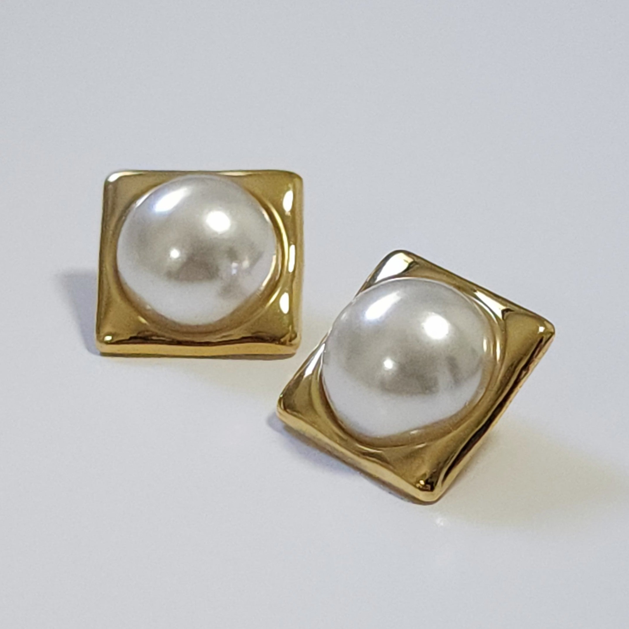 Pair of pearl earrings with gold square frames on a light gray background