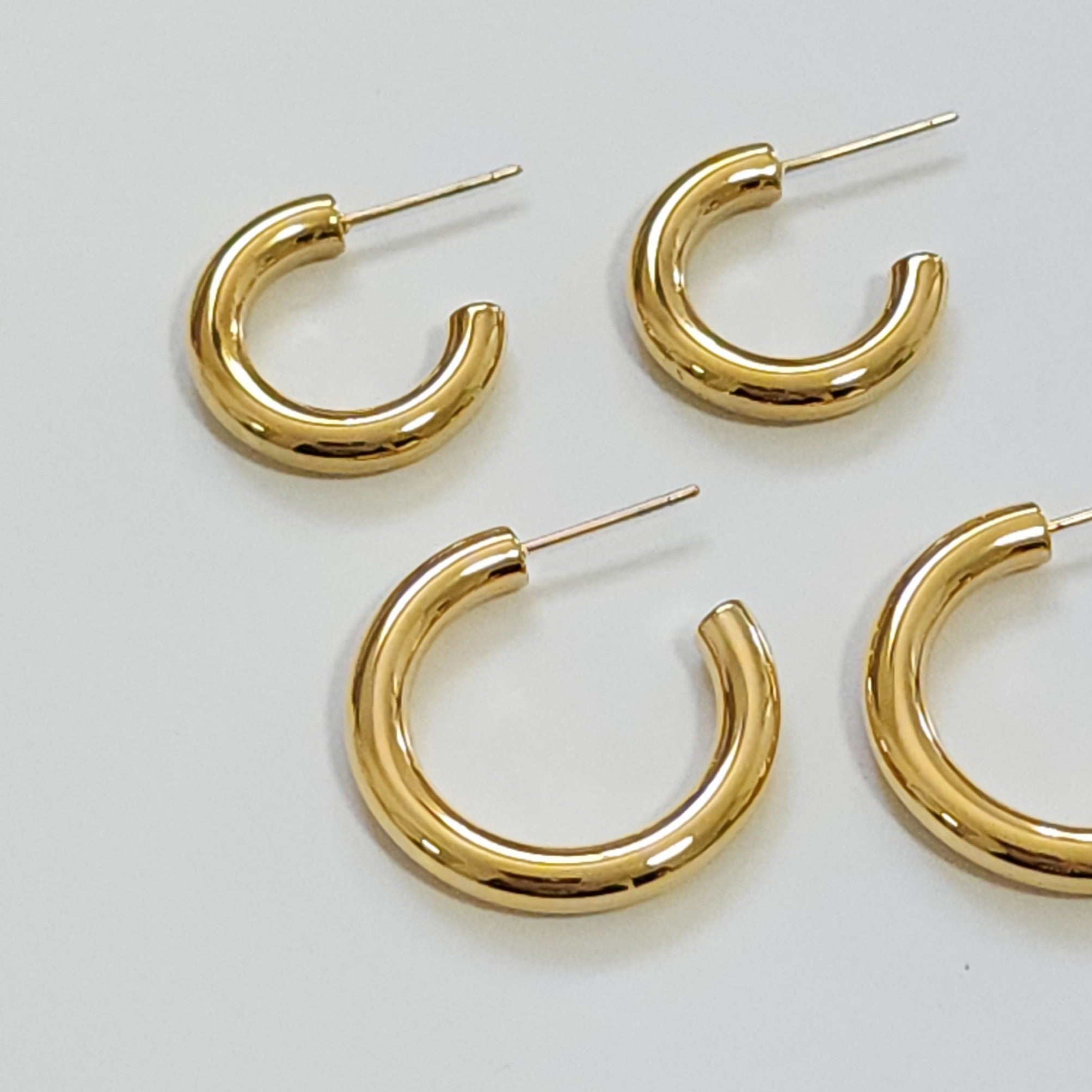 Four gold hoop earrings on a light gray background