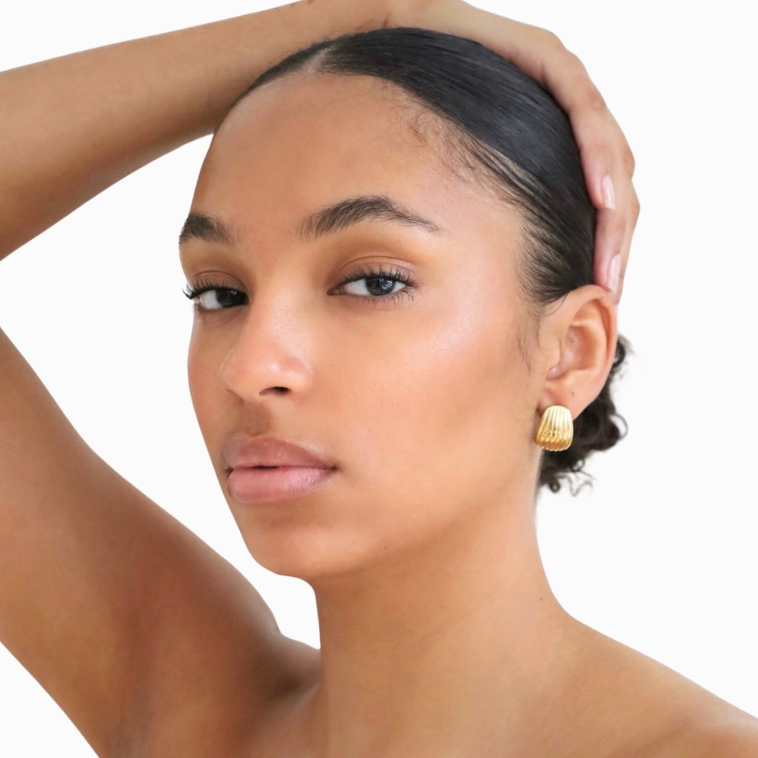 Woman wearing small gold stud earrings on a light grey background.