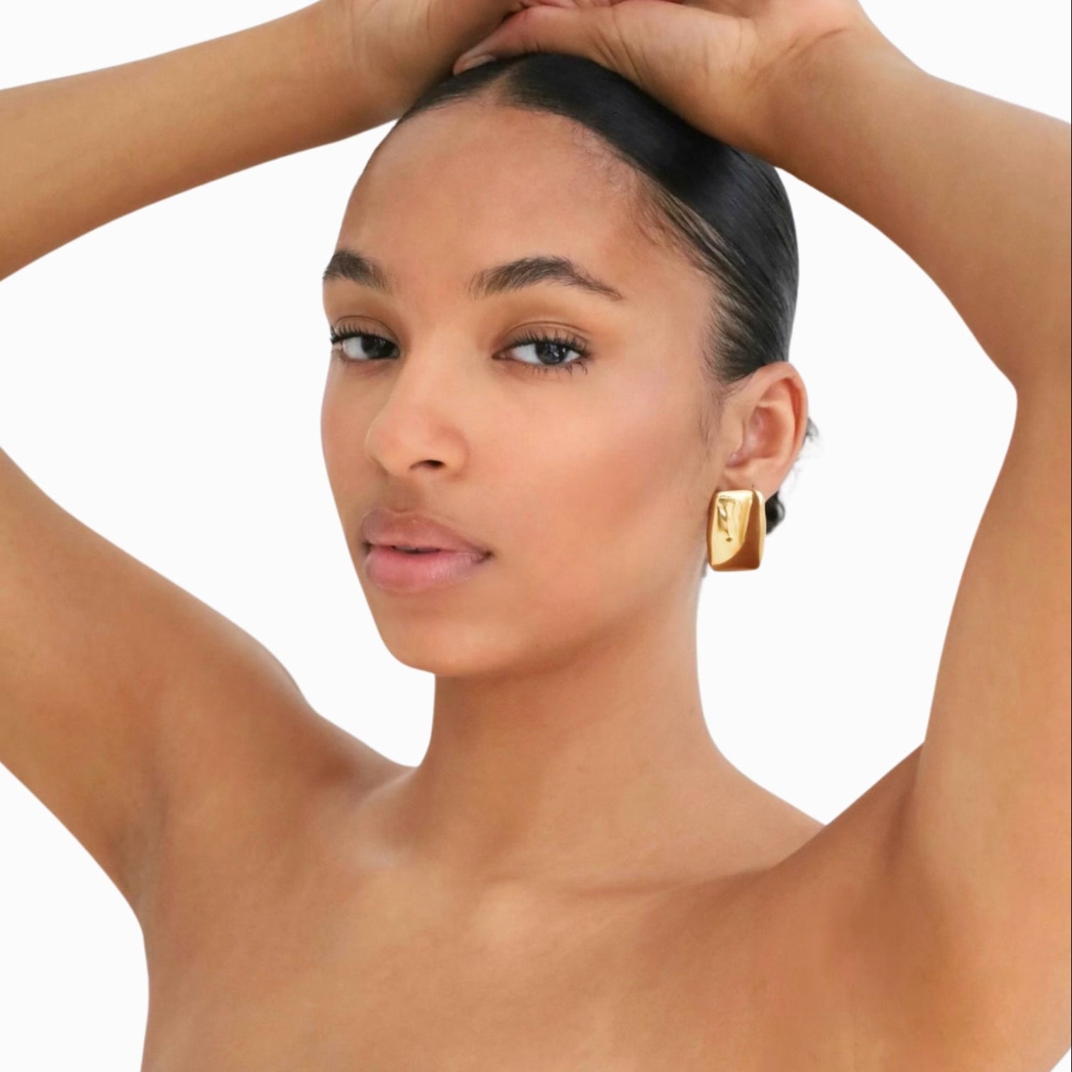 Woman wearing gold earrings with a plain background