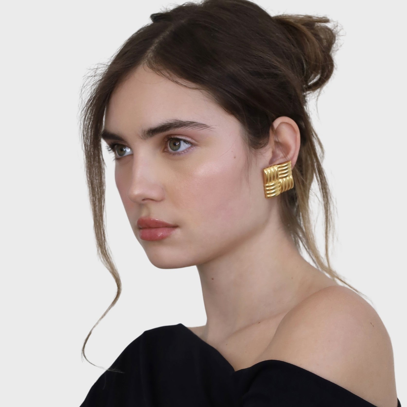 Woman wearing square gold statement earrings and a black top.