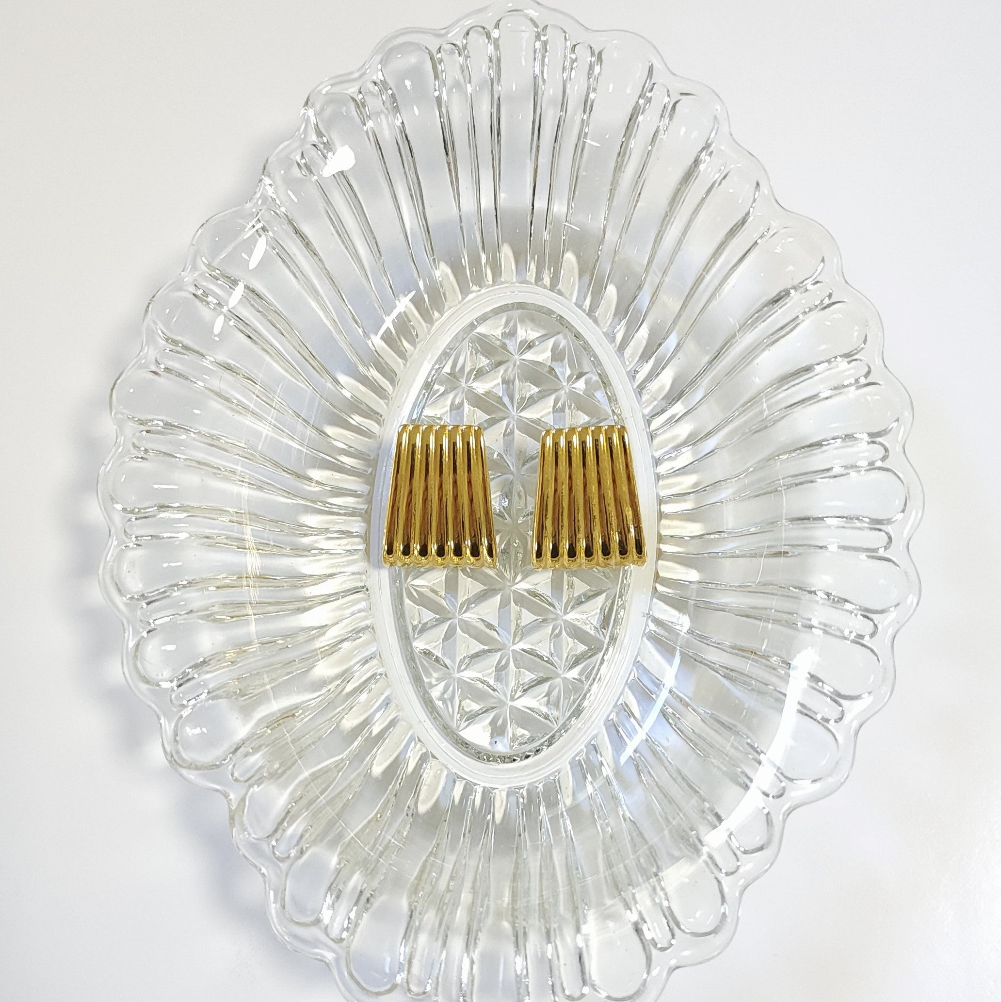 Gold vintage statement earrings on a clear glass dish with a white background