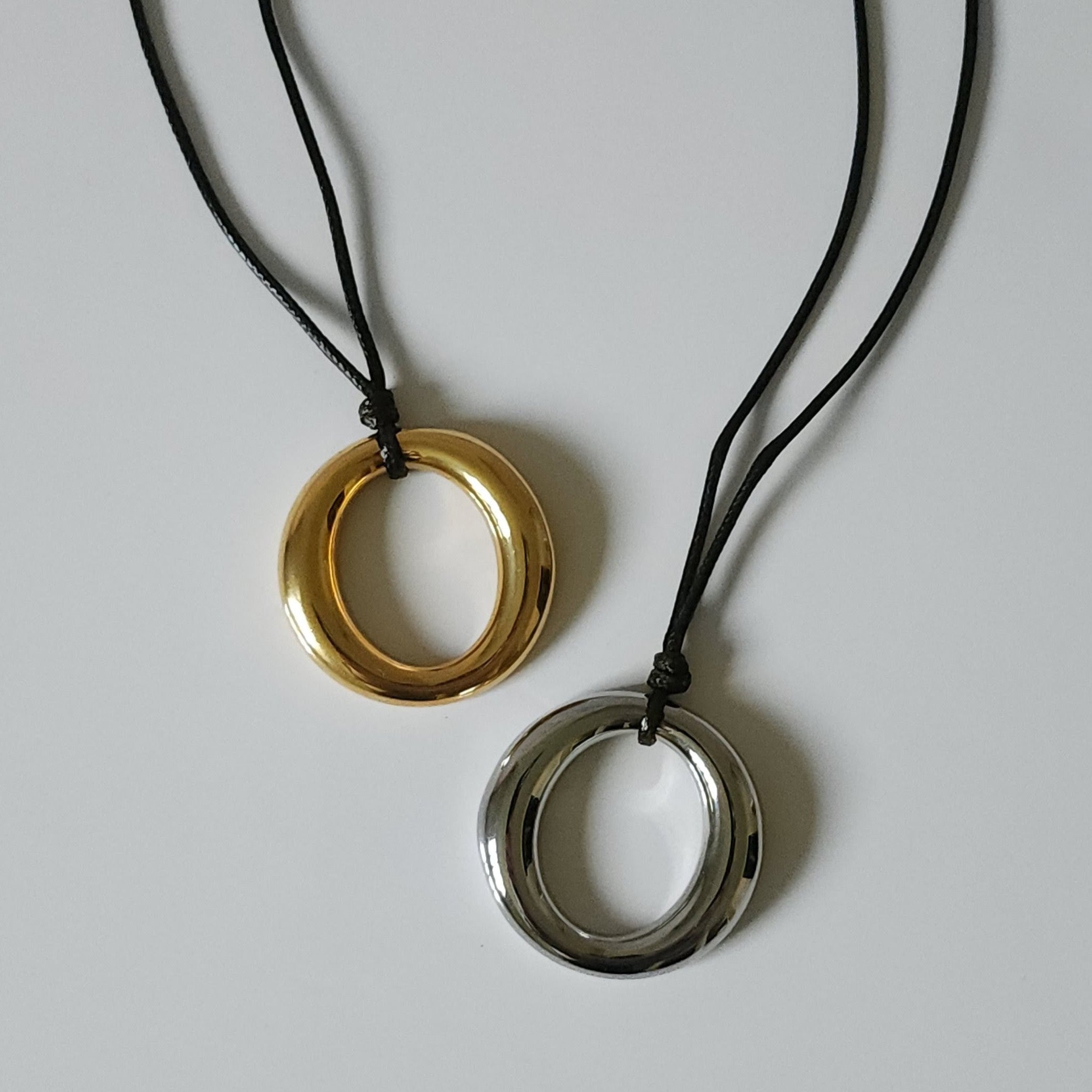 Two circular pendants on black cords against a light gray background