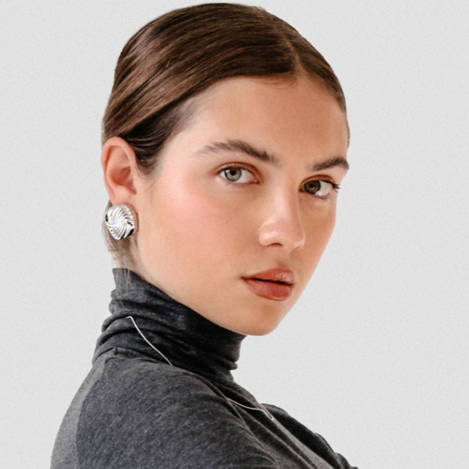 Woman wearing silver square statement earrings and a dark grey turtleneck on a light background.
