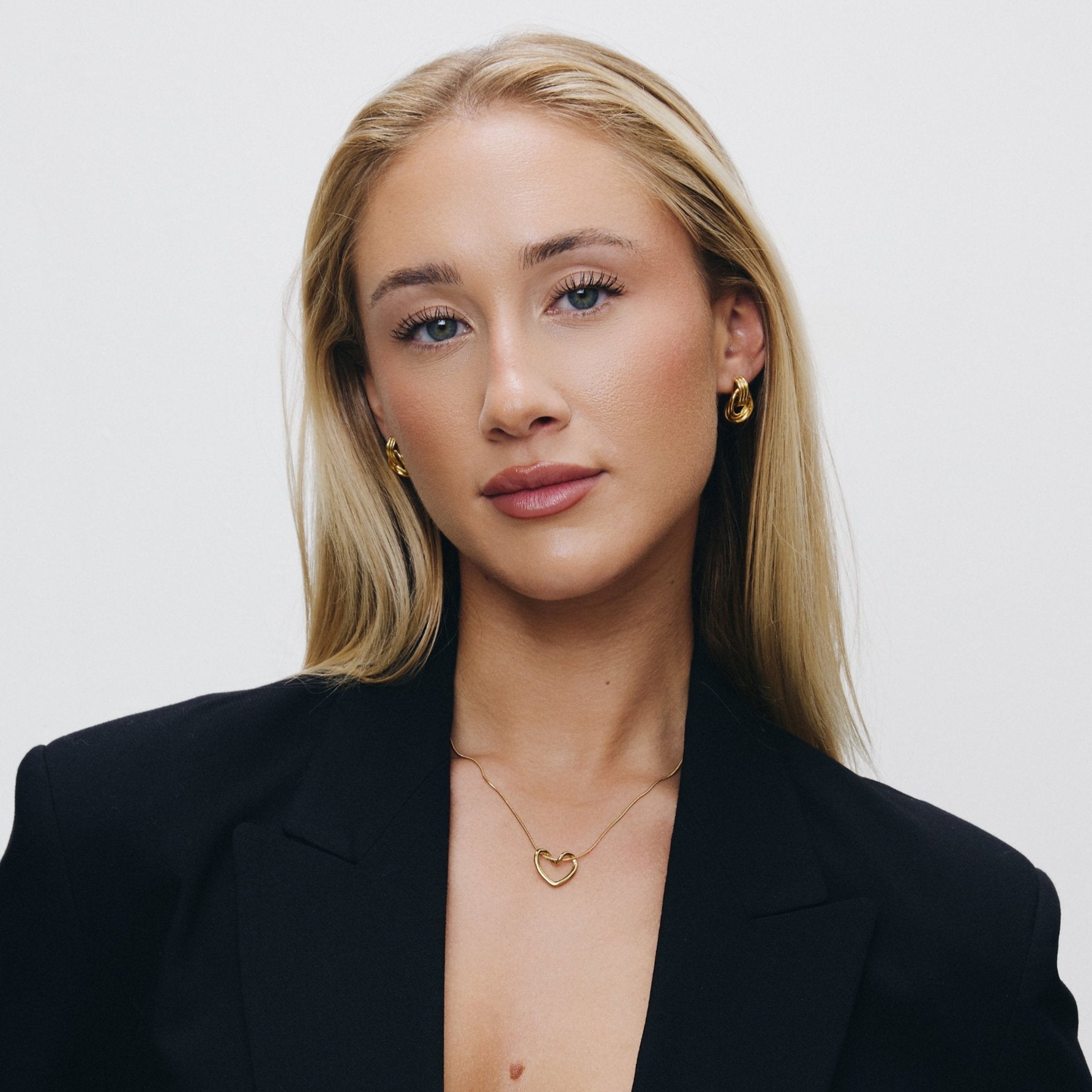 Women wearing heart pendant necklace with a black blazer against a white background.