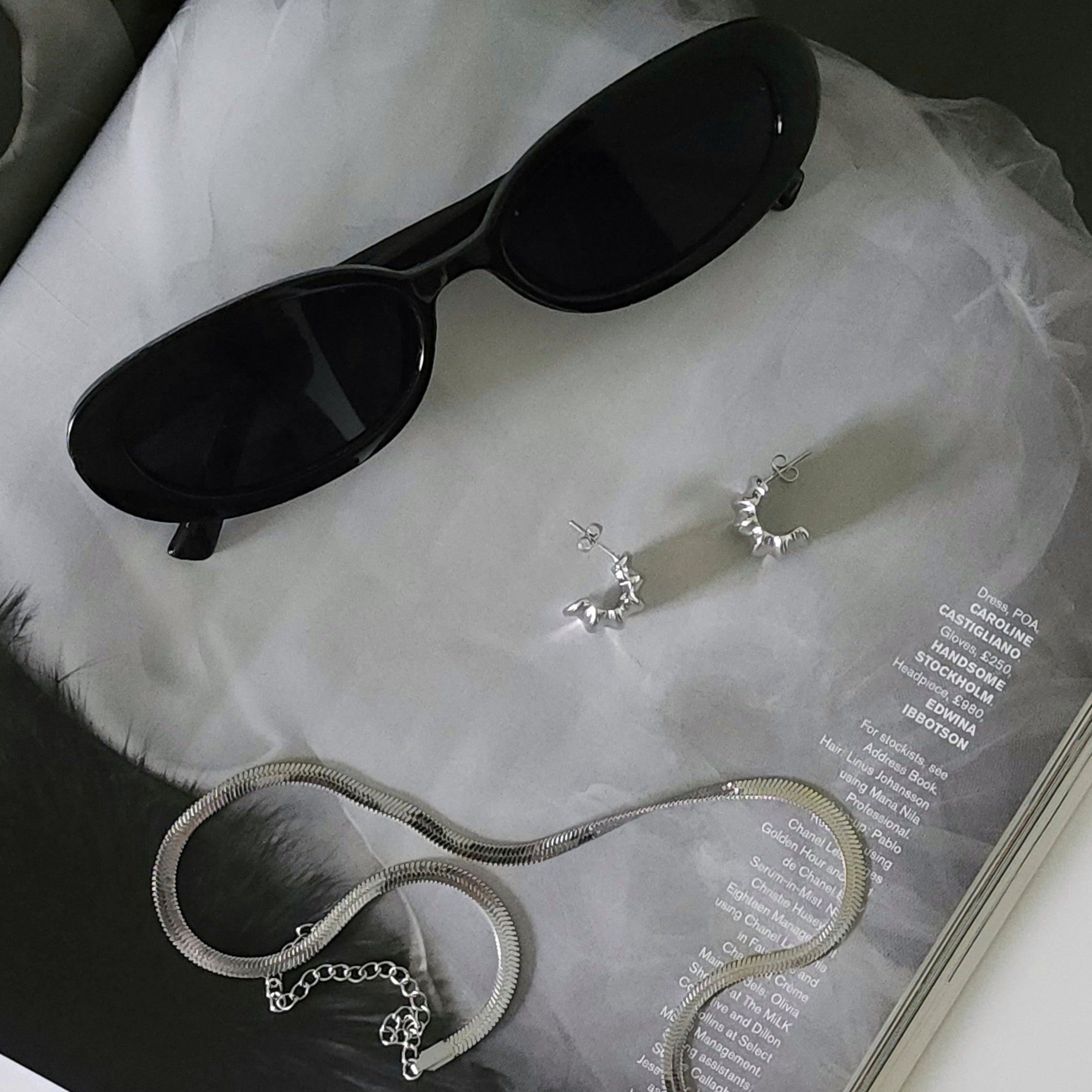 Gabriel Abstract Hoop Earrings in silver, silver necklace, and black sunglasses on a magazine