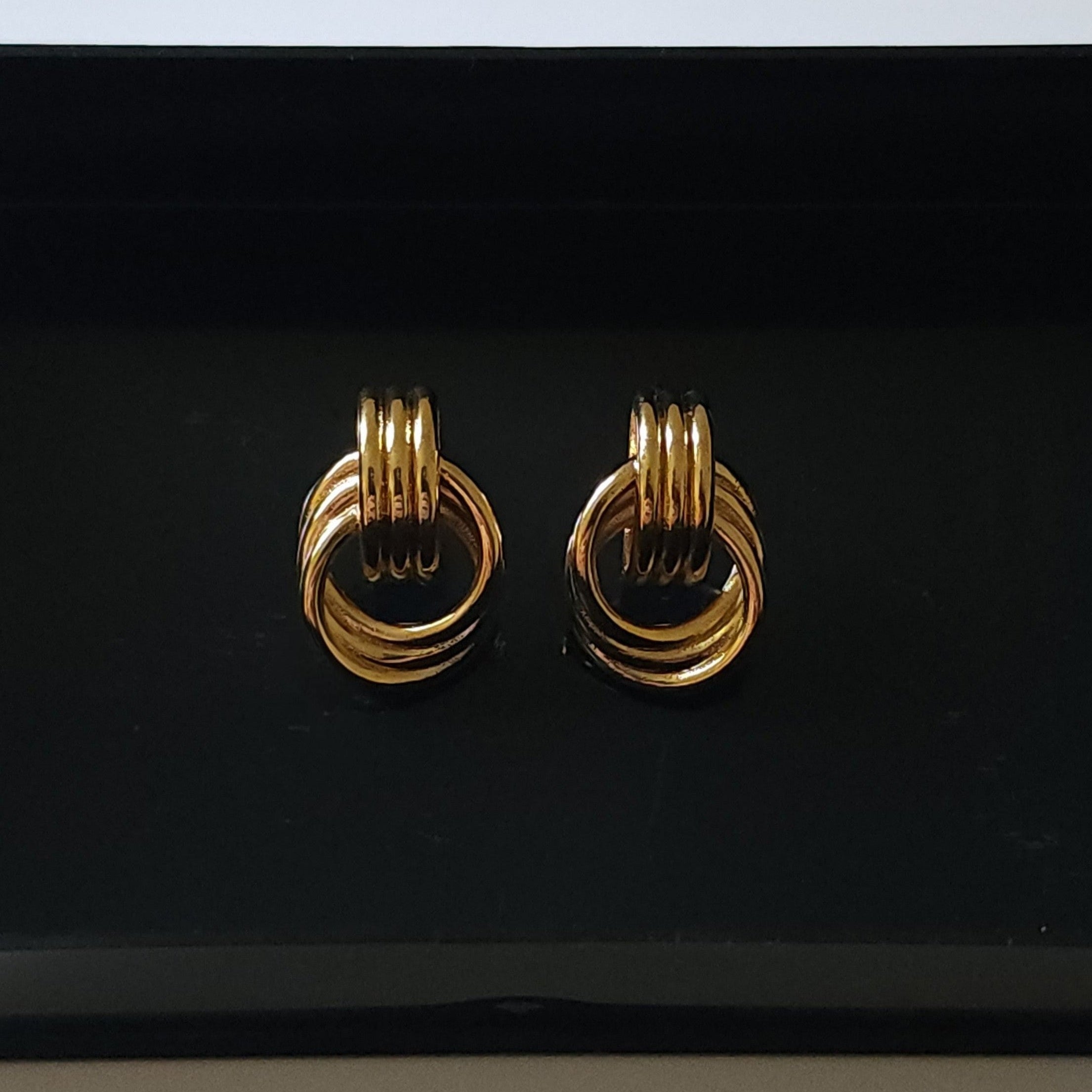Gold knot stud earrings on a black background.