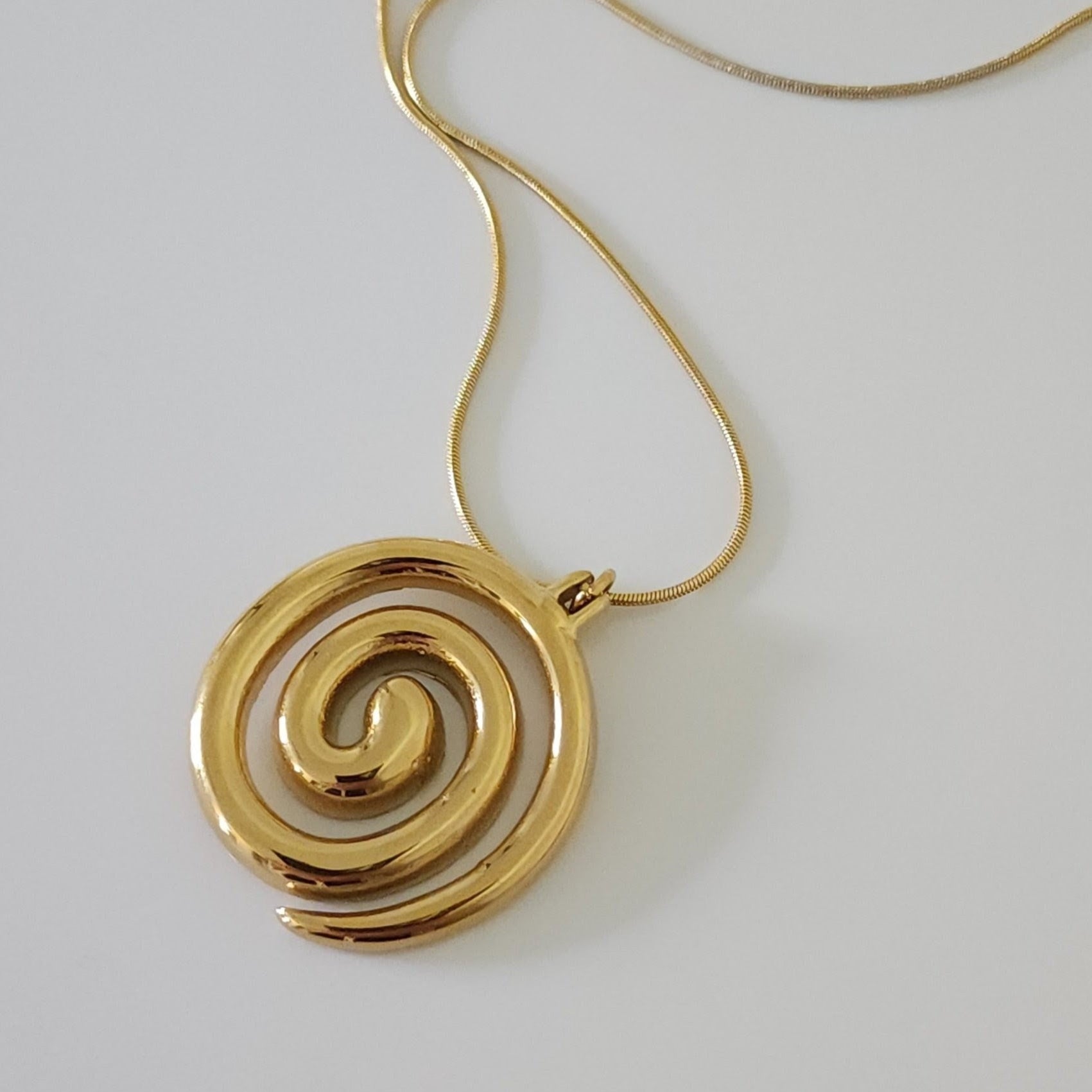 Gold spiral pendant necklace on a light gray background
