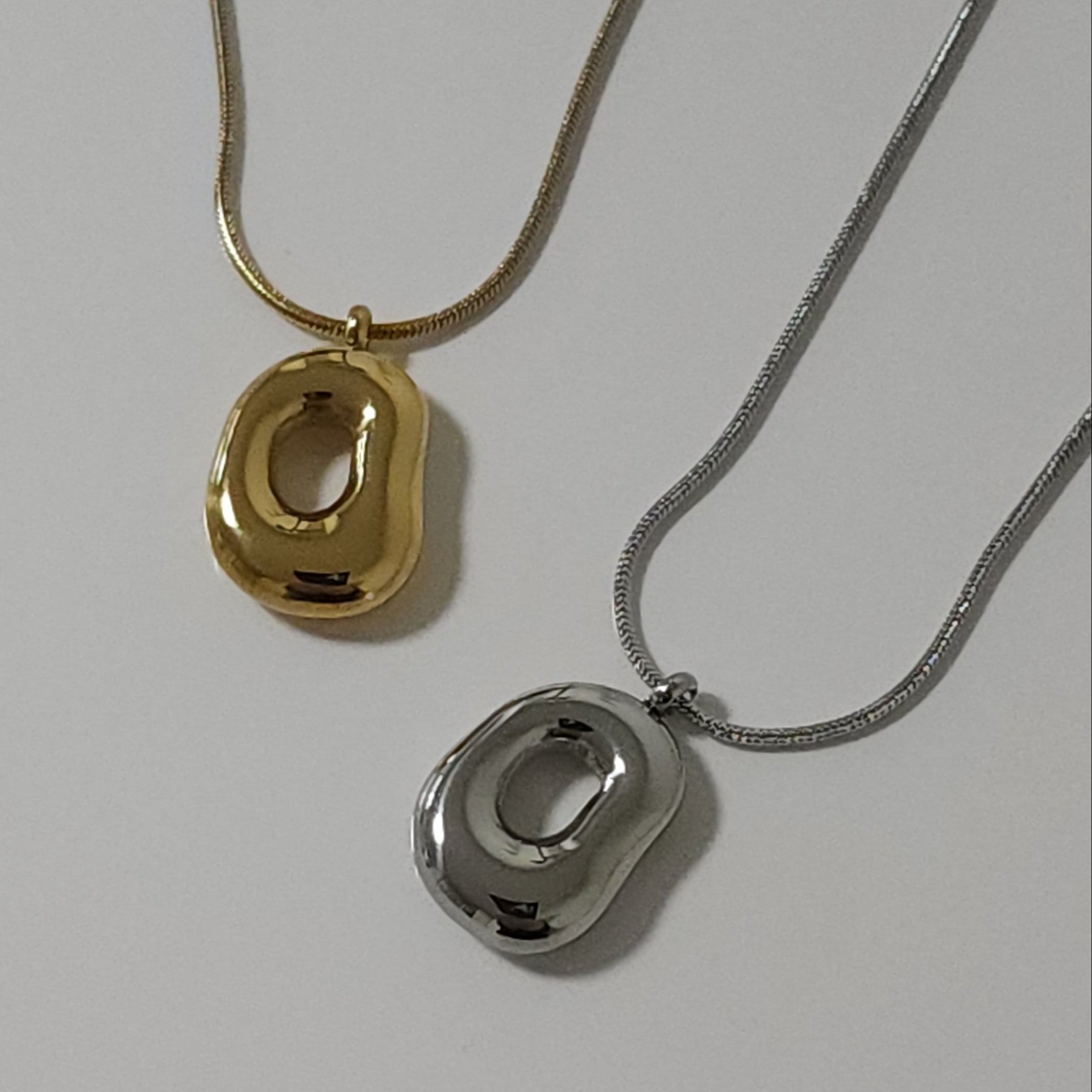 Two gold and silver necklaces with unique pendants on a light gray background