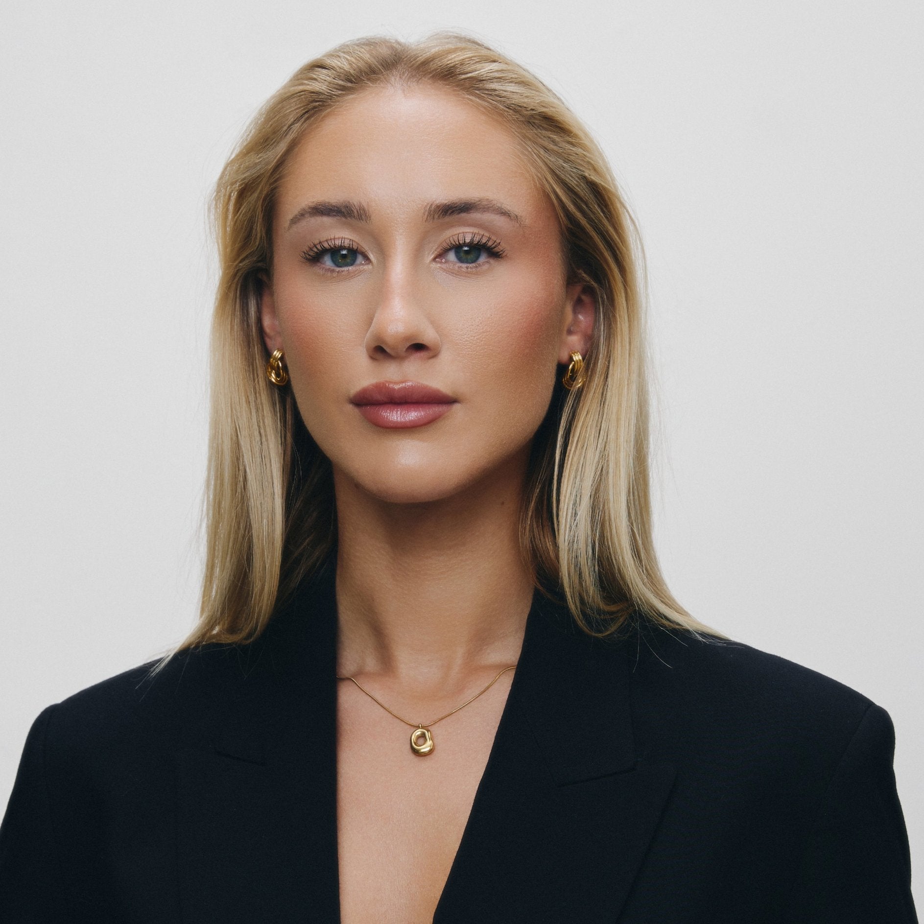 Woman wearing pendant necklace and a black blazer against a light background.