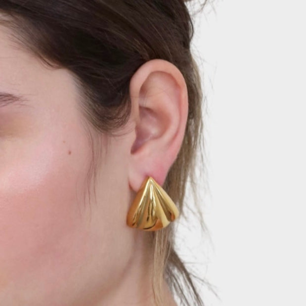 Close up image of gold statement earrings on woman's ear.