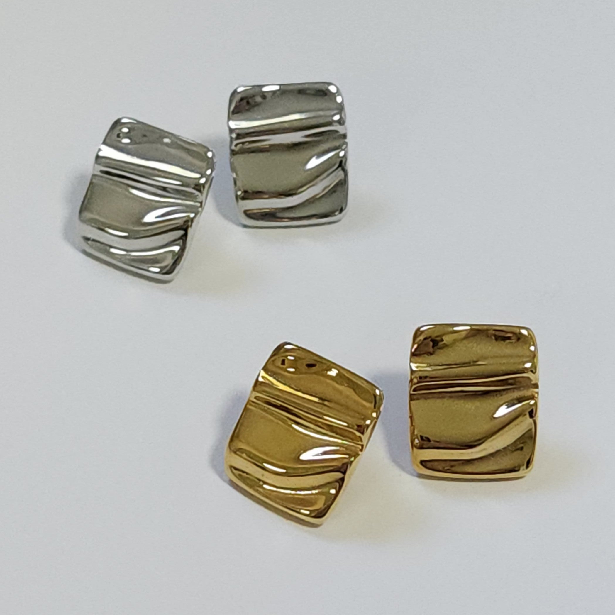 Two pairs of gold and silver earrings on a light gray background