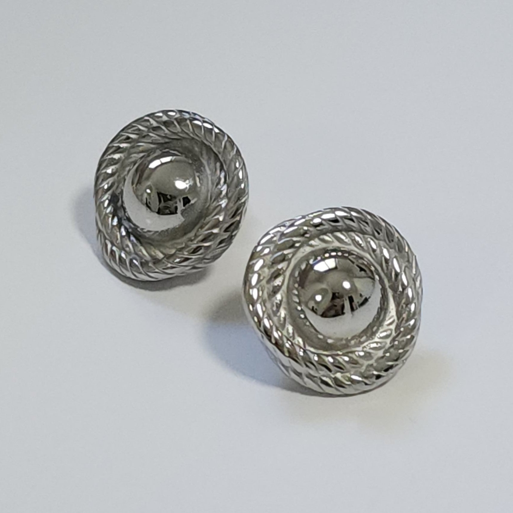 Pair of silver statement earrings with rope-like design on a light gray background