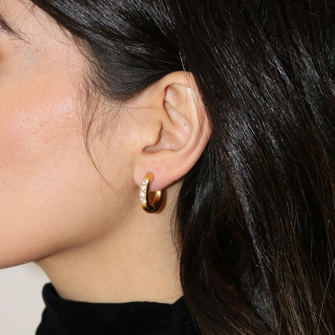Close up image of woman wearing gold hoop earrings with cubic zirconia settings.