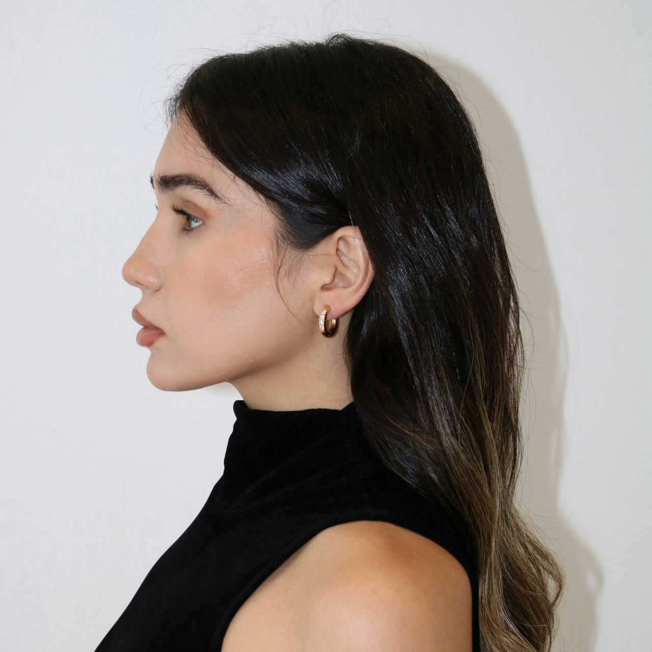 Woman wearing gold hoop earrings with cubic zirconia settings.
