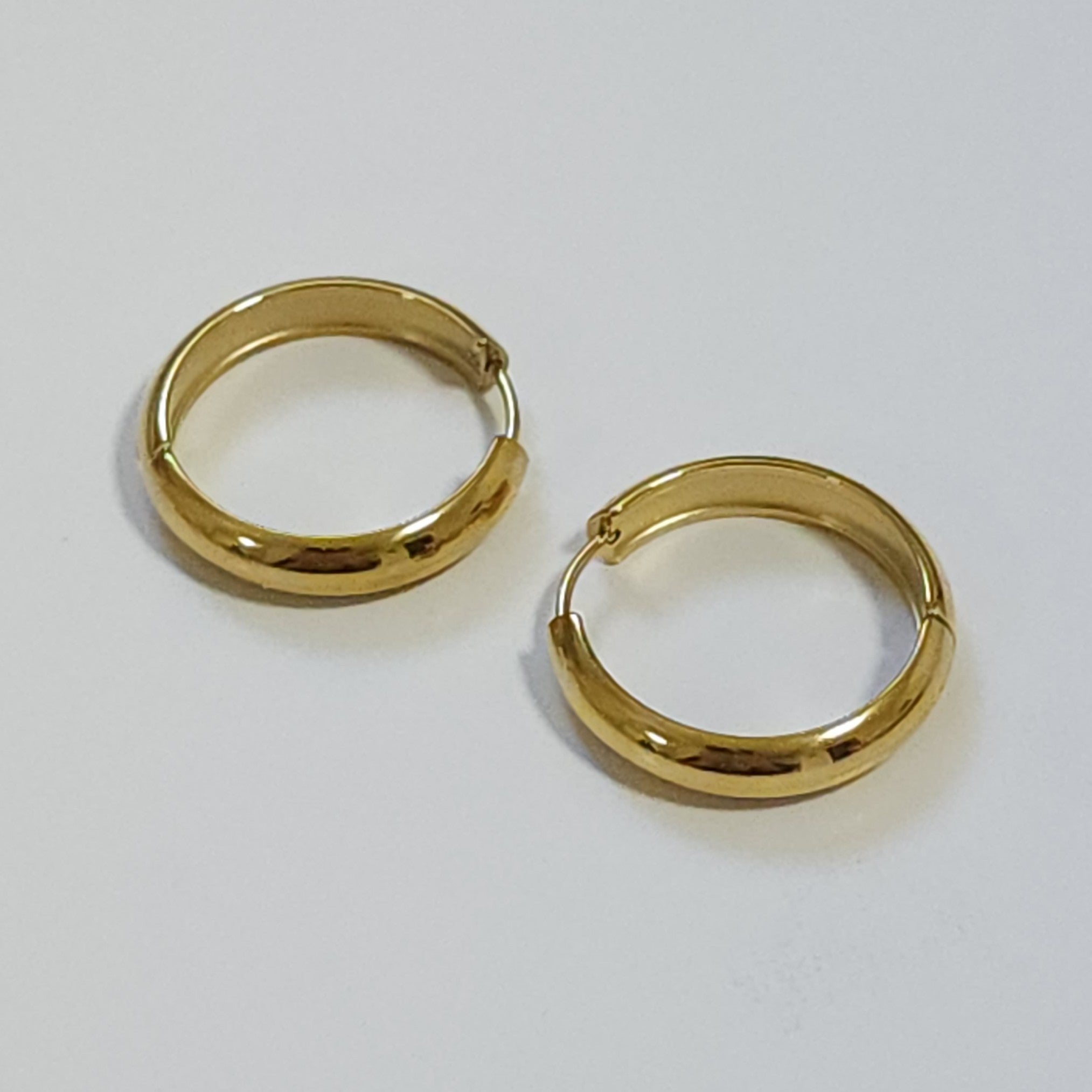 Pair of gold hoop earrings on a light grey background.