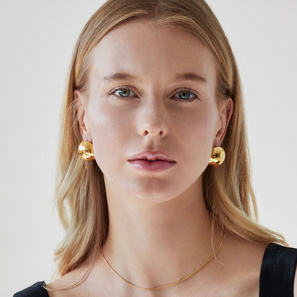 Woman wearing Yvette Mirrored Statement Earrings in gold with a dainty gold necklace and black tank top