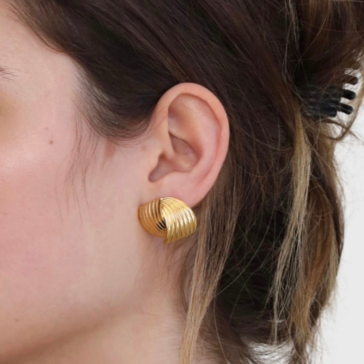 Close up image of gold stud earrings on woman.
