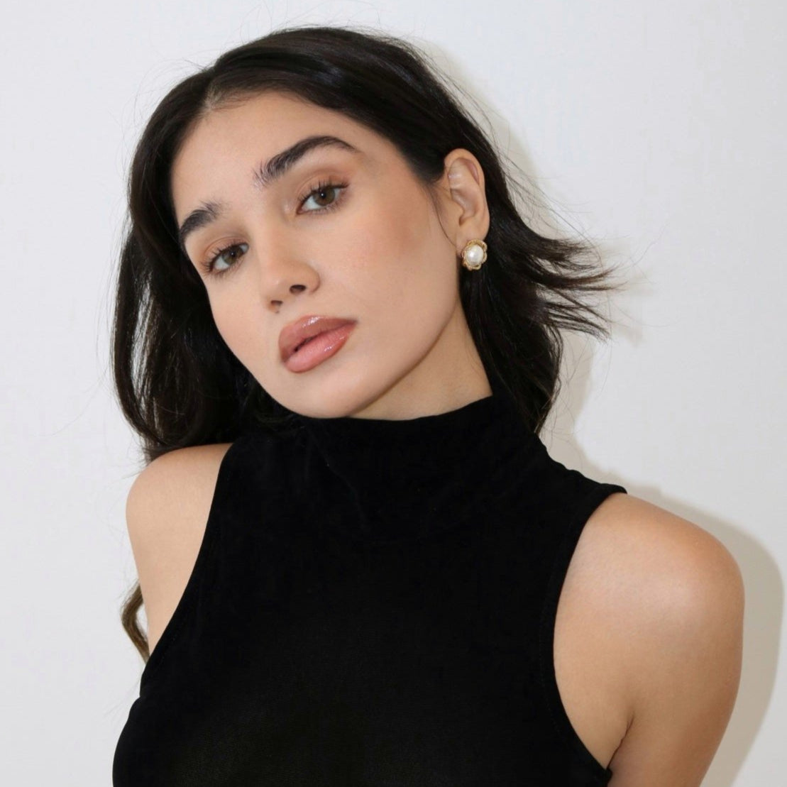 Woman wearing pearl stud earrings and  a black tank top against a light background. 