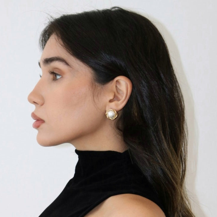 Woman wearing pearl stud earrings and  a black tank top against a light background. 