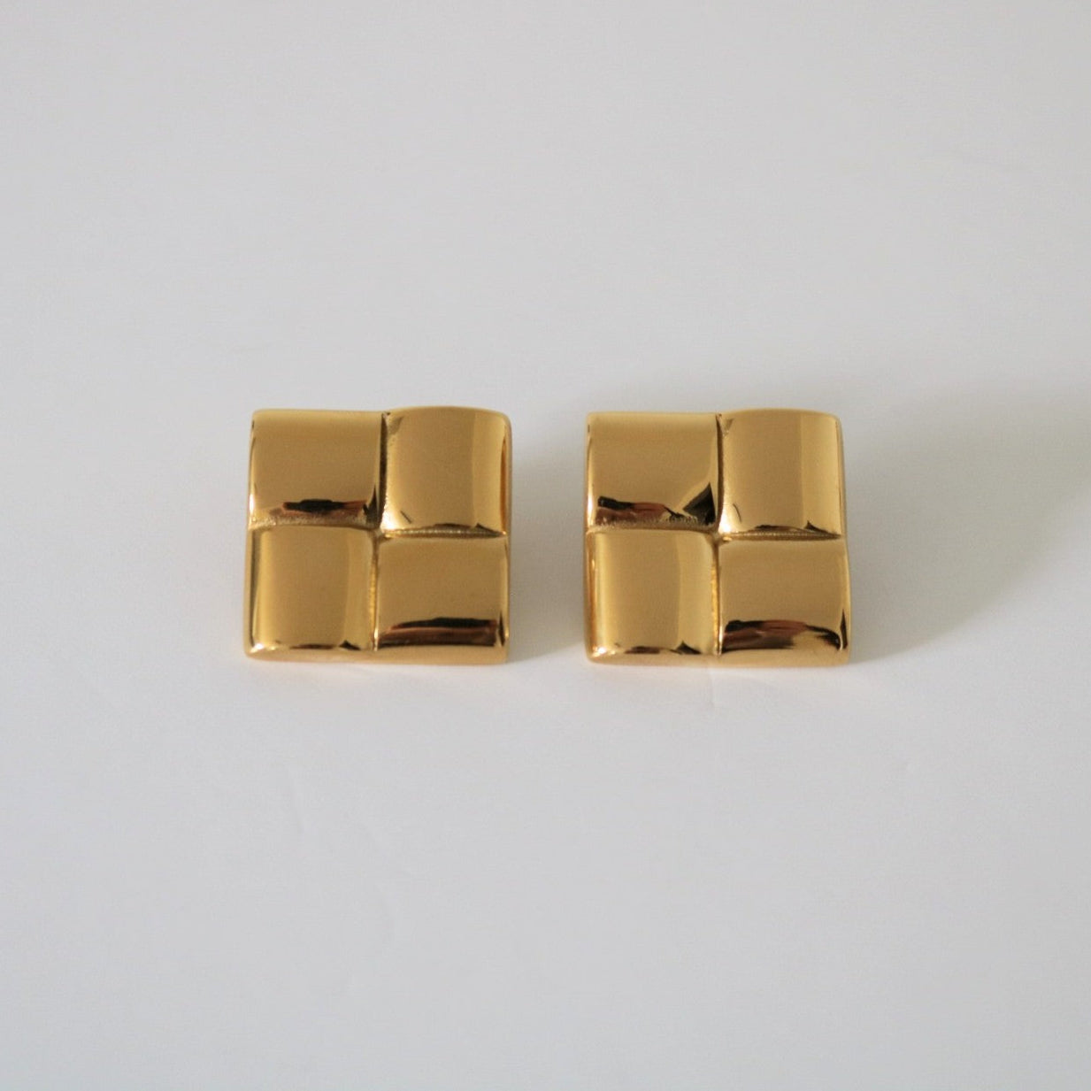 Pair of gold square earrings on a light gray background
