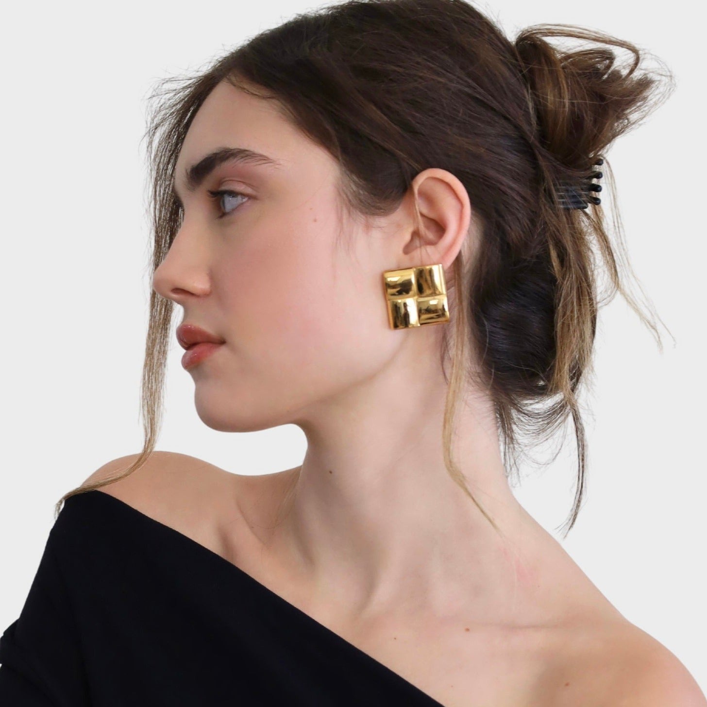 Woman wearing gold square statement earrings and a black top.