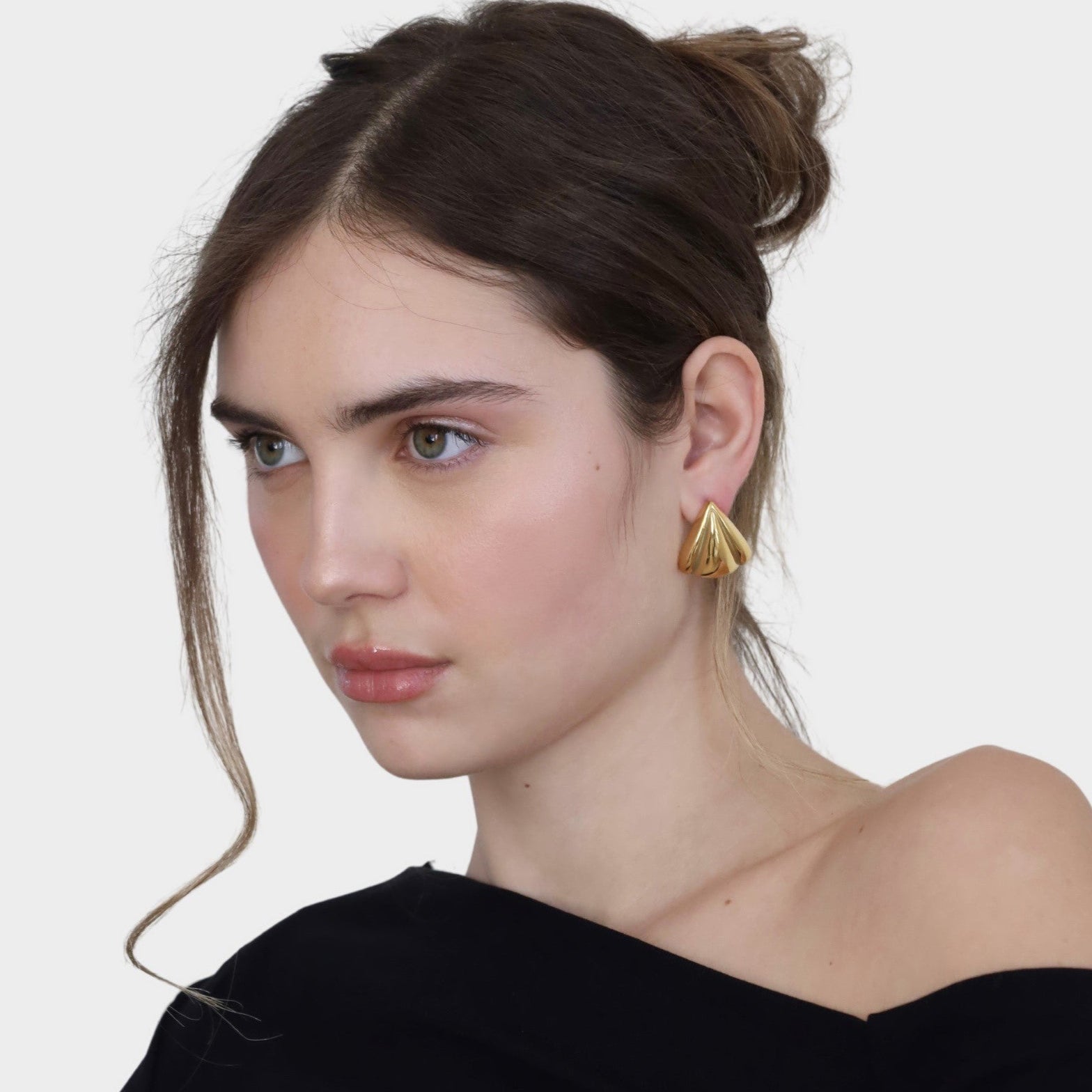 Woman wearing gold petal-shaped statement earrings with a black top.