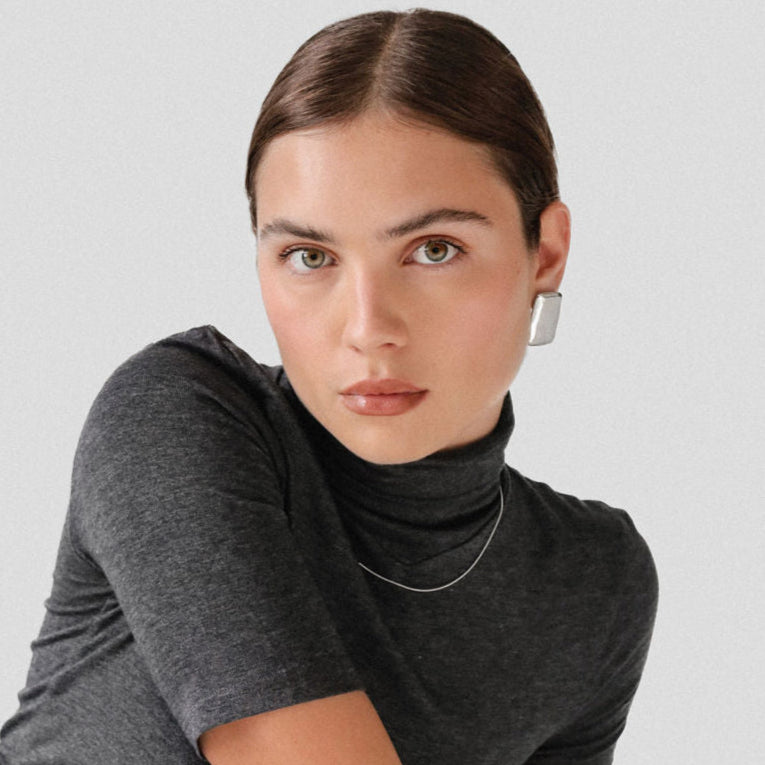 Woman wearing a gray turtleneck and silver earrings against a light gray background
