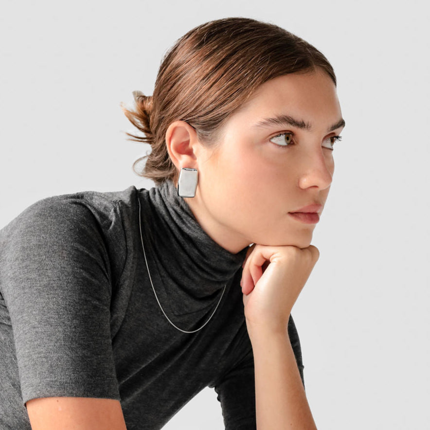 Woman wearing silver statement earrings and a grey turtleneck.