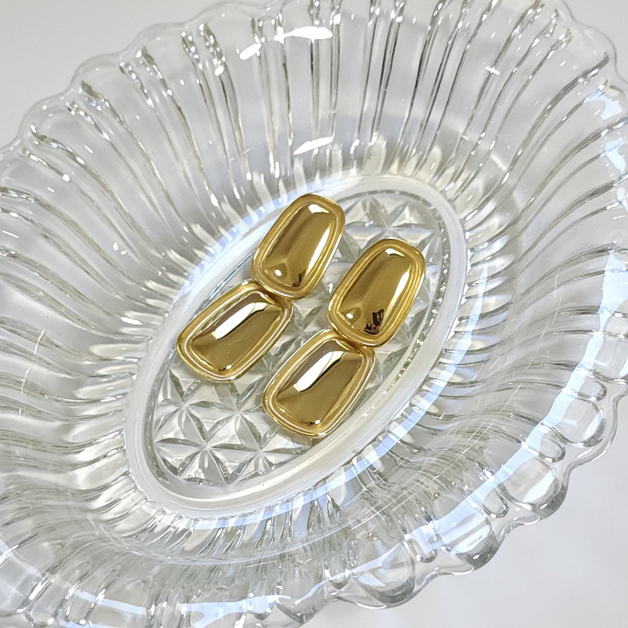 Gold earrings on a clear glass dish with a white background