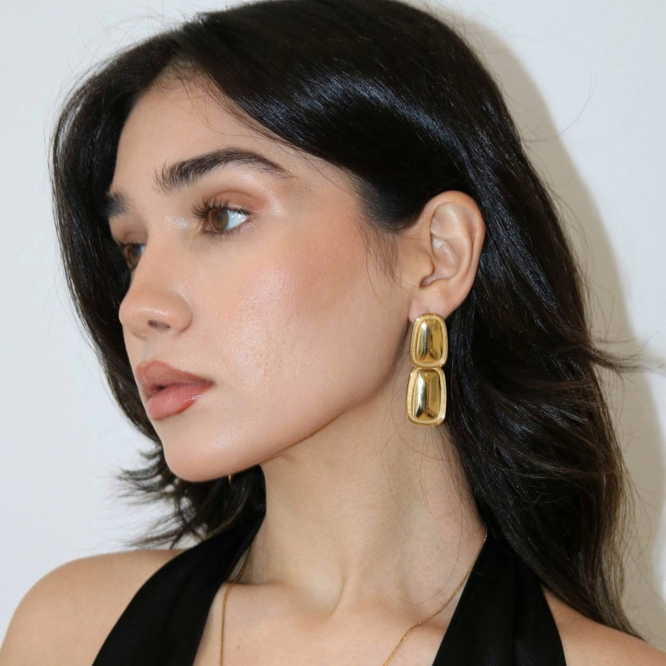 Woman wearing gold statement earrings and a black tank top.
