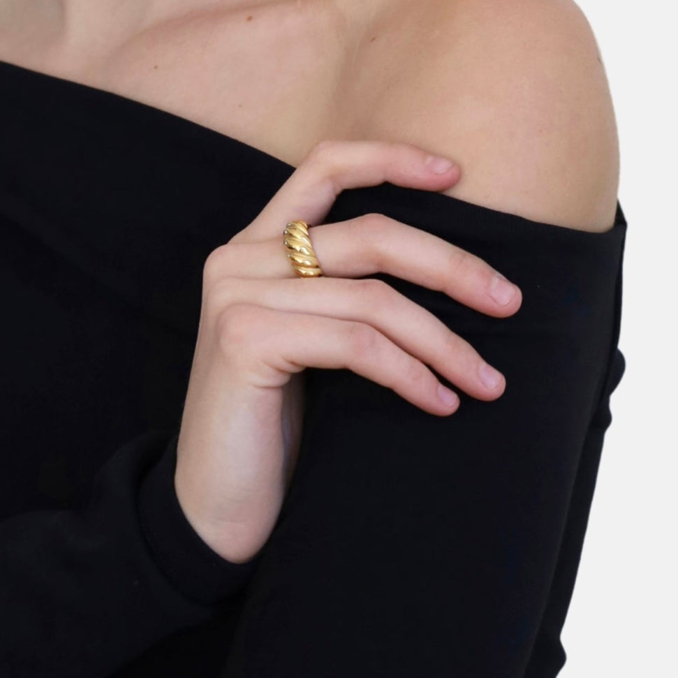 Close-up of a hand wearing a gold ring with a black off-shoulder top on a white background
